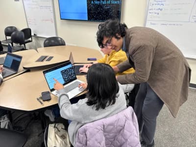 person bent down on circular table helping person on a laptop